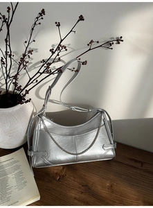 Primer plano del bolso plateado con textura plisada y detalle de cadena metálica elegante