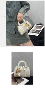 Detail view of cream Boston bag featuring star and cartoon charms with dual top handles
