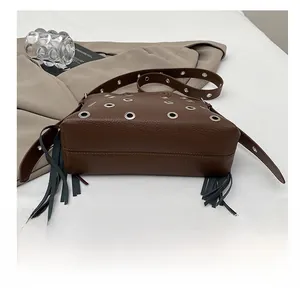 Dettaglio del fondo della borsa in pelle marrone con occhielli in metallo e nappe lunghe