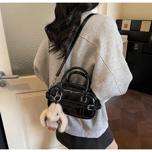 Detail of black patent leather handbag featuring silver buckle and plush bunny charm
