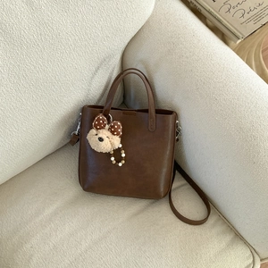 Détail du sac à main marron en similicuir avec breloque ours mignon sur un canapé doux