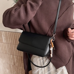Détail d'un sac bandoulière noir avec perles en bois sur une tenue de mannequin chic