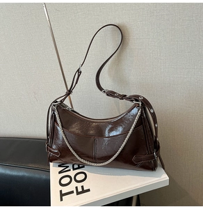 Detalle de bolso de hombro en cuero marrón oscuro brillante con cadena plateada y correa