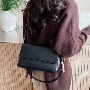 Détail du sac à bandoulière noir mat avec breloque vintage et fine bandoulière