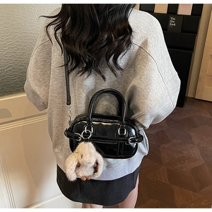 Detail of black patent leather mini handbag with a cute beige plush bunny keychain
