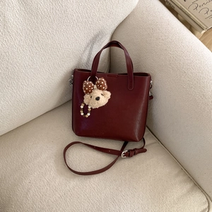 Détail du sac vintage bordeaux avec charme d'ours en peluche sur canapé blanc