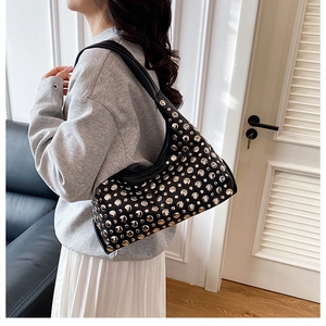Detail einer schwarzen Hobo-Tasche mit Nieten, von einem Model in einem Raum getragen