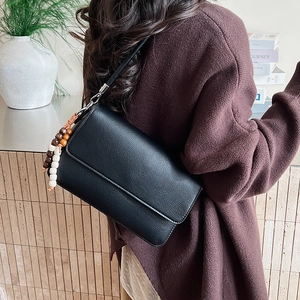 Détail du sac à main en cuir grainé noir avec pompon en bois vintage et boucles argentées
