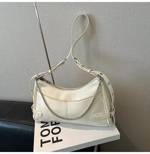 Detalle de bolso de hombro crema con cadena plateada y correa ancha decorada con tachuelas