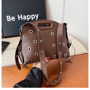 Dettaglio borsa in pelle martellata marrone con occhielli metallici e tracolla larga