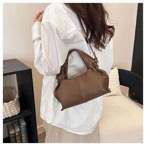 Detail view of deep brown cloud pleated bag worn on shoulder in a minimalist room