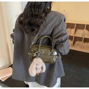 Detail of glossy olive green square handbag with plush bunny charm and round handles