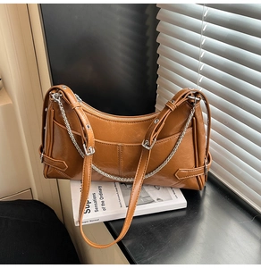 Detalle del bolso de cuero suave marrón con cadena metálica y hebilla de correa ajustable