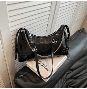 Detalle de bolso de hombro en cuero brillante negro con cadena plateada y correas