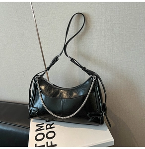 Detalle de bolso hobo negro brillante con cadena plateada y hebilla lateral ajustable