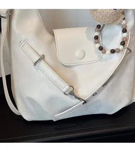 Detail der cremefarbenen Hobo-Tasche mit Ledertextur, Perlenkette und Plüschtier