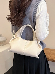 Chic beige cloud bag made of soft leather, worn as an underarm shoulder bag by a model