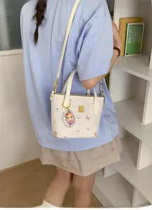 Dettaglio della borsa tote bianca con stampa cucciolo rosa, logo oro e ciondolo viola