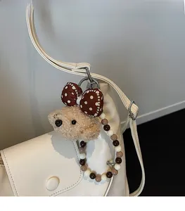 Detail eines Plüschbär-Anhängers mit gepunkteter Schleife an einer weißen Ledertasche