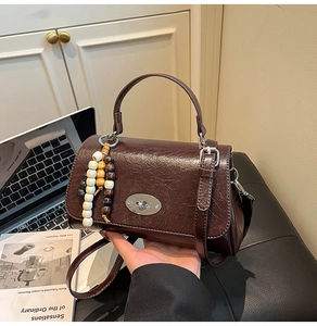 Detail of dark brown wrinkled leather handbag with silver twist lock and wooden bead charm