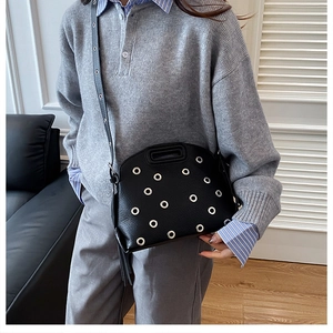 Dettaglio di borsa in pelle nera con occhielli argentati indossata da una modella