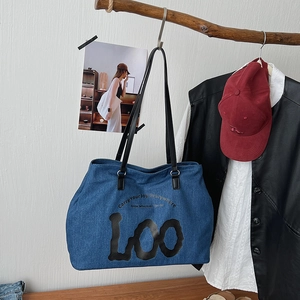 Blue denim tote bag with black logo hanging on a wooden hook against a white wall