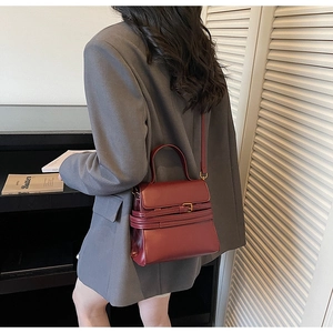 Détail d'un sac à main en cuir bordeaux porté par un mannequin en costume gris chic