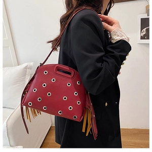 Dettaglio della borsa in pelle rosso scuro con occhielli in metallo e nappe con frange