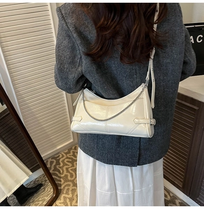 Modelo con un elegante bolso de hombro en charol beige con detalles de cadena metálica