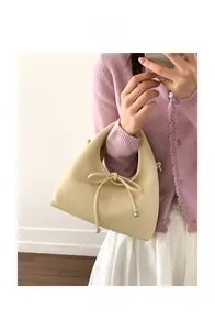 Detail showing creamy beige handbag with bow drawstring and silver beads on model