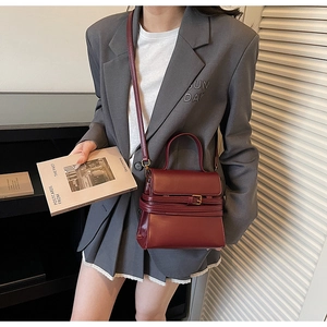 Détail d'un sac à main bordeaux en cuir porté avec un costume gris dans un décor sobre