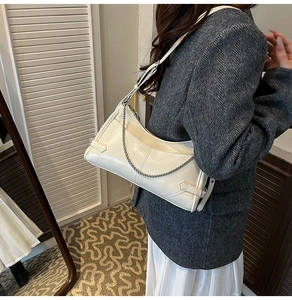 Detalle de bolso de hombro en cuero crema con cadena plateada y paneles cosidos