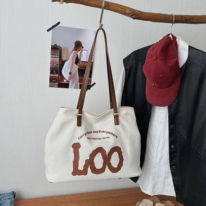 Detail view of large white canvas tote bag with brown leather straps and slogan text