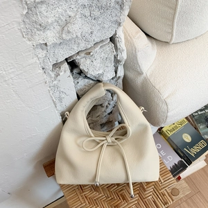 Close-up of cream white lychee texture handbag with delicate bow detail and metal accents