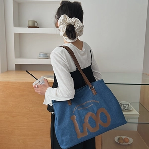 Detail view of large blue denim tote bag with brown straps worn on shoulder