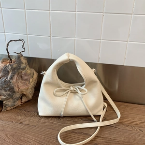 Detail of creamy white litchi grain leather shoulder bag with bow knot on wood desk