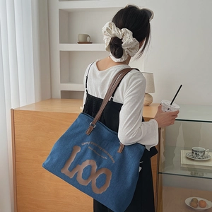 Detail of blue denim tote bag with brown leather handles and graphic slogan print
