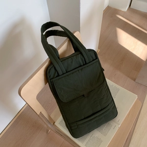 Detailed view of dark green quilted crossbody bag with front pocket on wooden chair