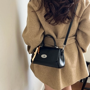 Detail of black crossbody bag with wooden bead charm and silver turn-lock closure on camel coat