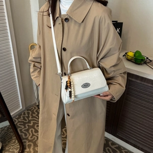 Detail of white textured leather crossbody bag featuring metal turn-lock and wood bead charm