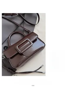 Detail shot of brown glossy leather bag with wide square buckle and braided strap detail