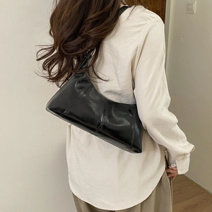 Close-up of a black glossy shoulder bag featuring distinct vertical stitching and reflective finish