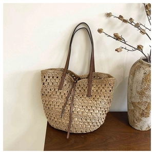 Detail of woven straw tote bag featuring brown leather straps and rustic interior lining