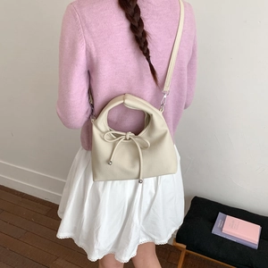 Detail of a beige leather dumpling bag with a delicate bow knot and adjustable strap