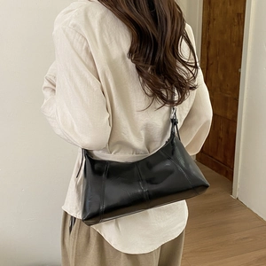 Model wearing a black glossy leather shoulder bag with decorative vertical stitching