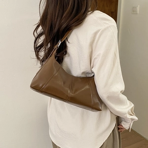 Detail of dark brown glossy leather underarm bag featuring vertical stitching on a model