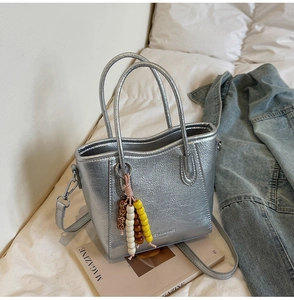 Detail of silver metallic tote bag with beaded charm and embossed fashion text