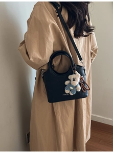 Détail du sac à bandoulière en cuir noir mat avec un charmant pendentif d'ours bleu
