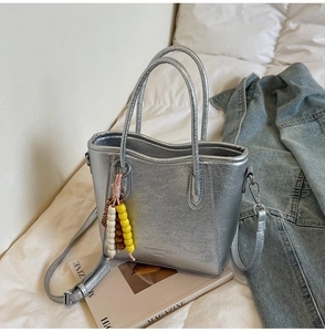 Detail of silver metallic bucket bag with colorful bead charm and long shoulder strap