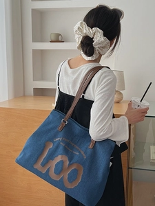Blue denim tote bag with brown leather straps and slogan print in a cozy cafe setting